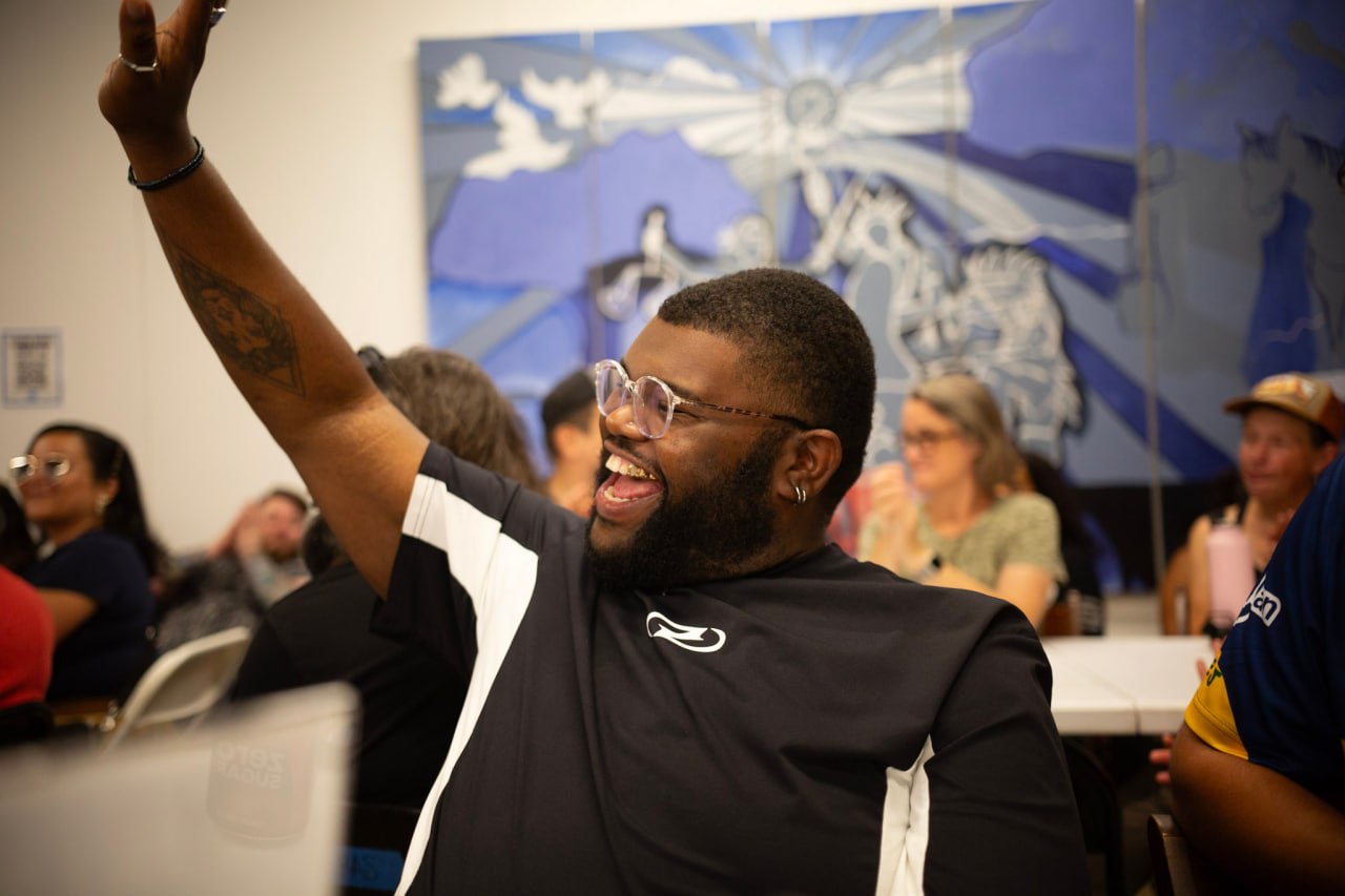 A community participant smiling and raising his hand during a gathering